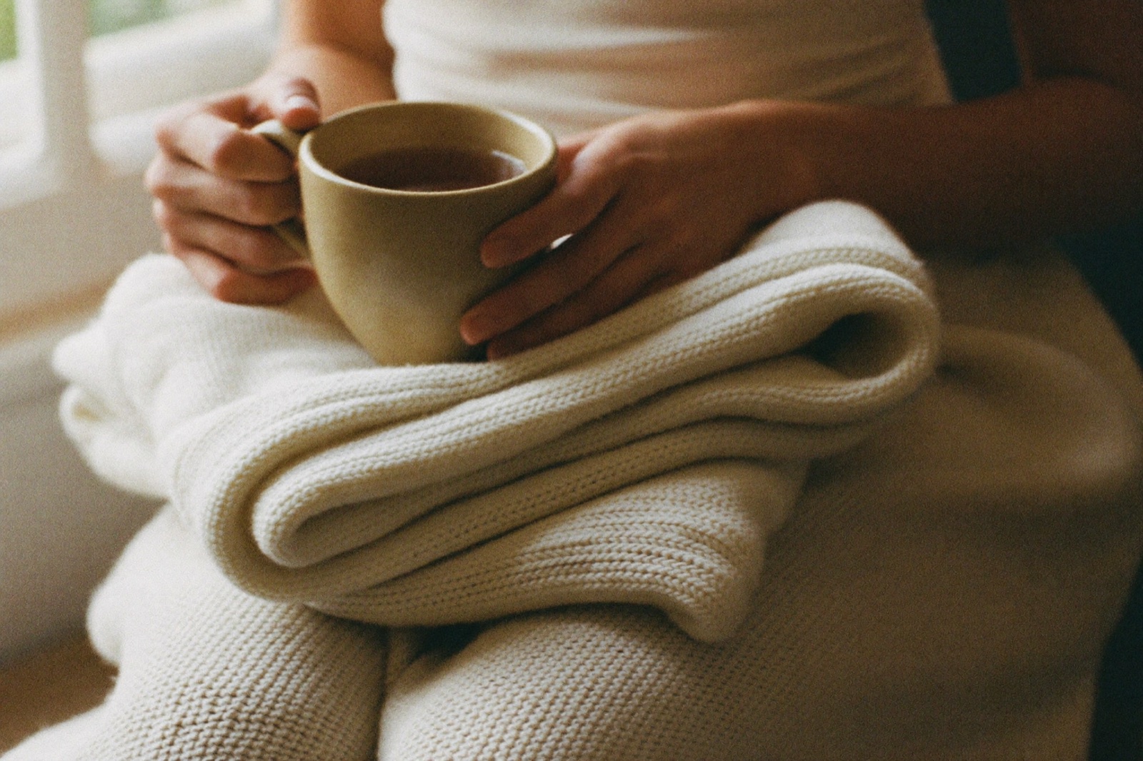 Unas manos sostienen una taza de infusión sobre una mantita de bebé doblada